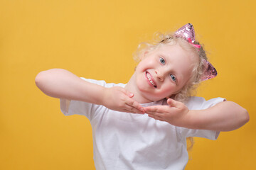 cute little girl in a white t-shirt having fun, a child in a headband with cat ears on a yellow...