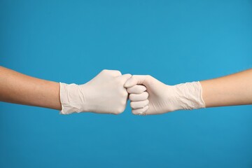 Doctors in medical gloves making fist bump on light blue background, closeup