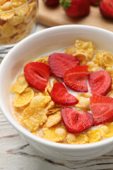 Bowl of tasty crispy corn flakes with milk and strawberries on white wooden table, closeup