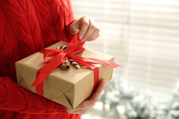 Woman holding Christmas gift box indoors, closeup. Space for text
