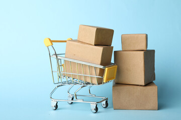 Shopping cart and boxes on light blue background. Logistics and wholesale concept