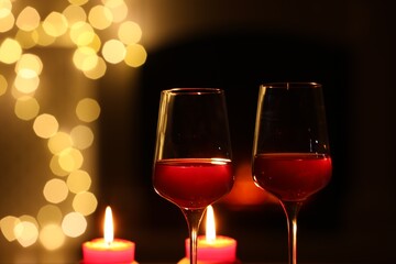 Glasses of wine and candles against blurred lights, closeup with space for text. Romantic dinner