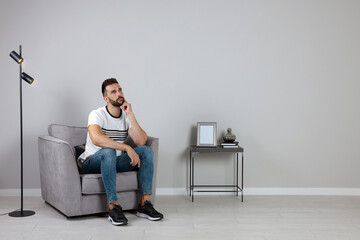 Man sitting in armchair near gray wall, space for text