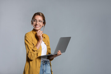 Portrait of young woman with modern laptop on grey background. Space for text