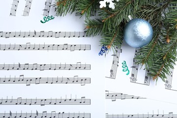 Fir branches and blue light blue ball on Christmas music sheets, flat lay