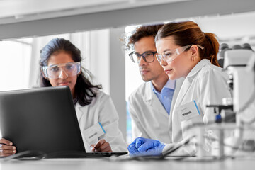 science research, work and people concept - international team of scientists with laptop computer working in laboratory - 525719219