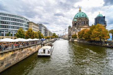 A tour boat alongside cafe patios on the Spree River at Autumn with the Cathedral in view in...