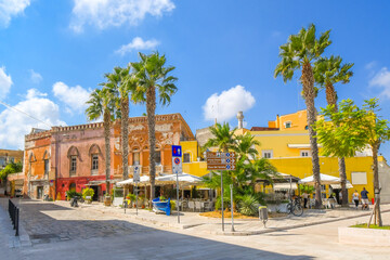 Fototapeta na wymiar The waterfront promenade at the port of Brindisi, Italy, with colorful shops, cafes and palm trees along the Mediterranean Sea in the Puglia region.