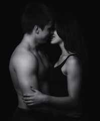 Young couple hugging and kissing as foreplay before having sex isolated on black background	