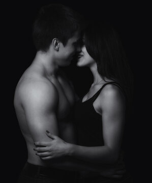 Young couple hugging and kissing as foreplay before having sex isolated on black background	