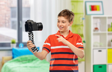 blogging, videoblog and people concept - portrait of happy smiling boy video blogger with camera and tripod videoblogging over home room background