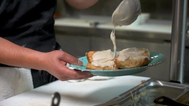 Cook ladles creamy white country gravy over toasted biscuits, slow motion 4K