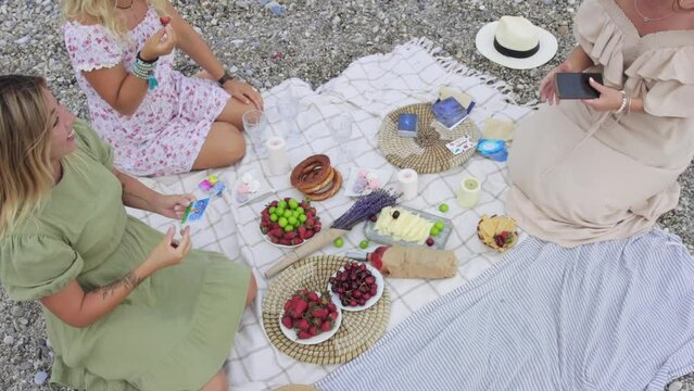 Four smiling women at a picnic by the sea playing a card game