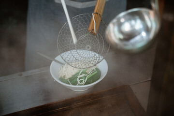 hands of seller pouring into the bowl of boiled noodles with a sieve from the pan