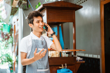 male merchant wearing apron makes a call using a mobile phone with cart background