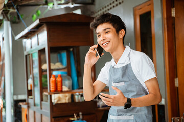 male chicken noodle seller wearing apron makes a call using a mobile phone with cart background
