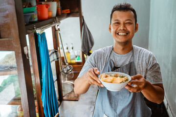 man seller smiling while bringing a bowl of chicken noodles for customers in a stall cart