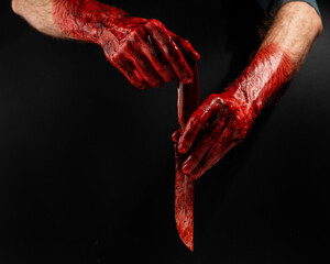 Man holding knife with bloody hand on black background. 