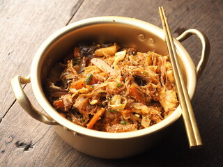 Stir fried glass noodles and mixed vegetables with Gochujang sauce, served in golden pot and with...