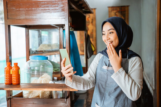 veiled woman wearing an apron surprised when she saw a cellphone while selling at a chicken noodle cart