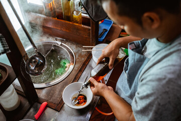 the seller prepares the spices and vegetable oil into the bowl while preparing the dish on the cart