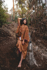 Portrait of sexy and young japanese woman with beautiful old traditional brown and orange kimono seated in a big tree trunk in the autumn forest