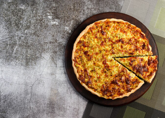 Leek and cheese pie on a round wooden cutting board on a dark grey background. Top view, flat lay