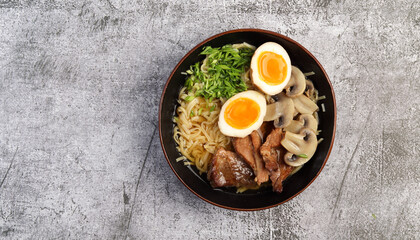 Japanese ramen with pork belly, mushrooms and marinated eggs in a a bowl on a dark grey background. Top view, flat lay