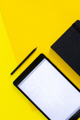 Home office flat lay with tablet and black notebook on yellow background