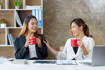 Two young Asian businesswomen join together for coffee and work discussion and share their job...