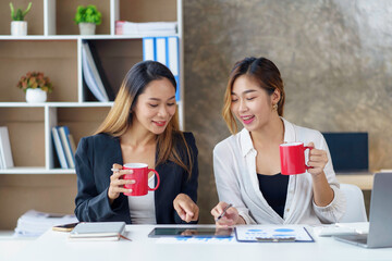 Two young Asian businesswomen join together for coffee and work discussion and share their job...