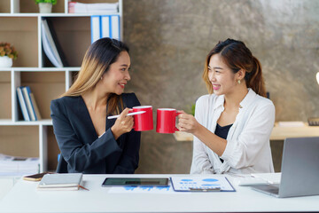 Two young Asian businesswomen join together for coffee and work discussion and share their job...