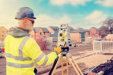 Site engineer in hi-viz working on house building construction site using modern surveying...
