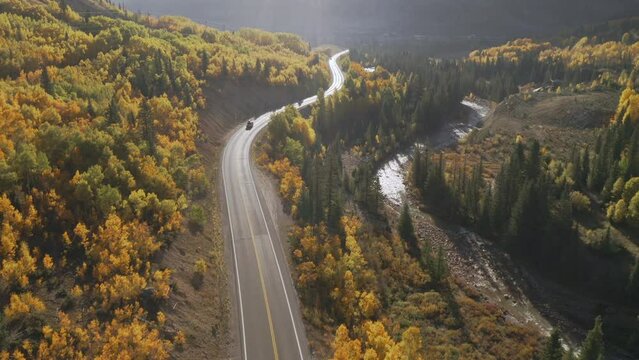 Aerial shot forward of beautiful Colorado mountain roads and bright yellow and orange aspen trees during autumn in the San Juan Mountains along the Million Dollar Highway road trip