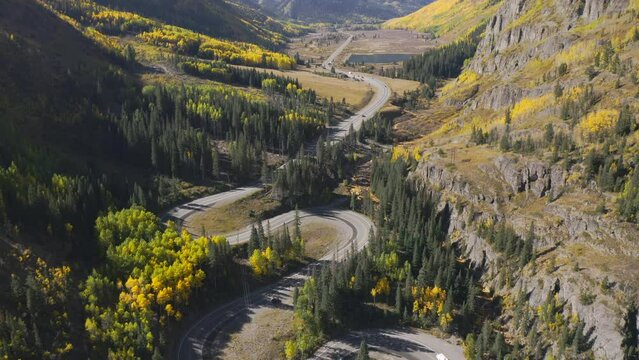 Aerial shot panning up of beautiful winding Colorado mountain roads and bright yellow and orange aspen trees during autumn in the San Juan Mountains along the Million Dollar Highway road trip
