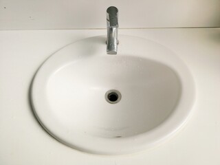White sink and silver faucet with water drop marks, old and dull image.