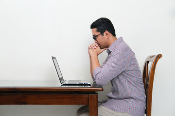 Side view of Asian man looking to his laptop with serious focus expression - Powered by Adobe
