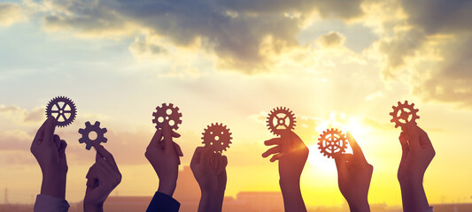 Hands holding of gear from at sunset sky background. teamwork industry concept.