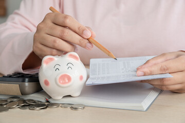 Woman save money in piggy bank and calculating book bank statement for household expense