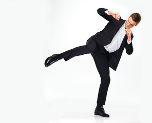 Business man doing a karate kick to the side while standing in a studio with copy space. Man in...