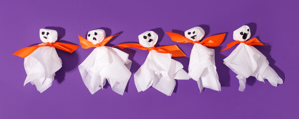 Decoration for Halloween party - ghosts from paper napkin and orange bow on traditional bright violet purple background, creative concept of night party, trendy hard shadow, flyer for promotion