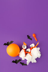 Halloween paper decorations on bright purple violet background. Black bats, ghosts, balloons. Halloween concept. Flat lay, top view, overhead. Party greeting card, invitation, flyer, banner