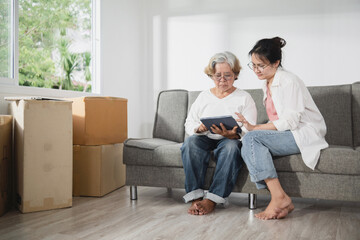 Concept of moving room and new house, Asian elderly woman and daughter. Talking and using a tablet.