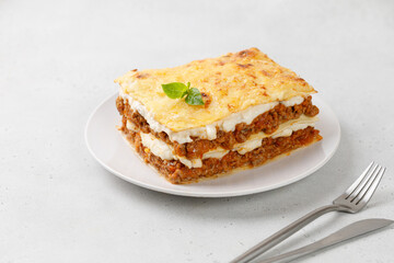 Traditional Italian lasagna. Delicious Lasagne with bolognese meat sauce and cheese on white plate with fork and knife. Copy space.