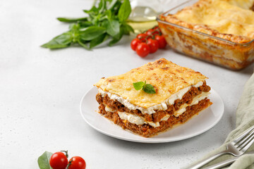 Delicious Lasagne with bolognese meat sauce and cheese on white plate with fork and knife. Traditional Italian lasagna. Copy space.