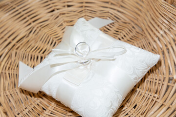 wedding rings on small white cushion silk pillow with ribbon on wooden wicker basket background
