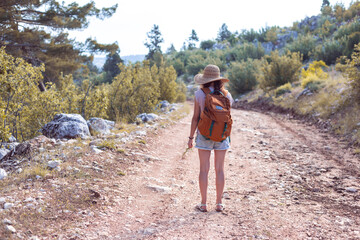 A woman with a backpack and a straw hat on a mountain path