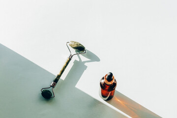 Serum bottle and jade facial roller on light blue background with shadows. Top view, copy space....