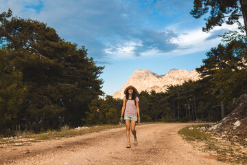 Obraz premium A girl with a backpack and a straw hat walks along a mountain path