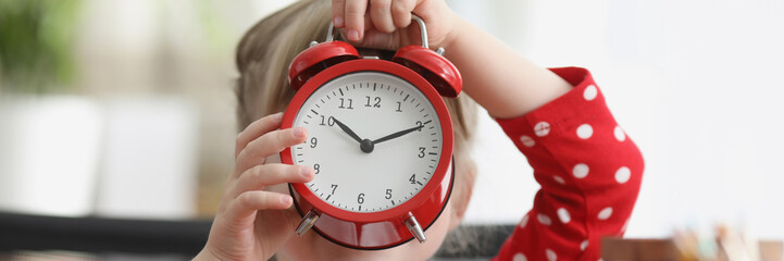 Little girl holding red alarm clock in front of her face